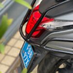 Close-up van het achtergedeelte van een scooter met rood achterlicht, bagagerek en blauwe kentekenplaat.