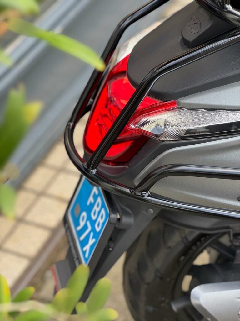 Close-up van het achtergedeelte van een scooter met rood achterlicht, bagagerek en blauwe kentekenplaat.