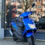 Blauwe scooter op standaard geparkeerd voor een winkelraam in de stad