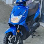 Blauwe SYM Orbit III scooter met schijfrem voor, geparkeerd op het trottoir