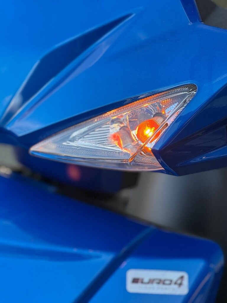 Close-up van een brandende oranje richtingaanwijzer op blauwe scooter met Euro4-sticker