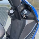Close-up van een blauwe scooter: sleutel in het contactslot op de middenconsole met zwarte panelen.