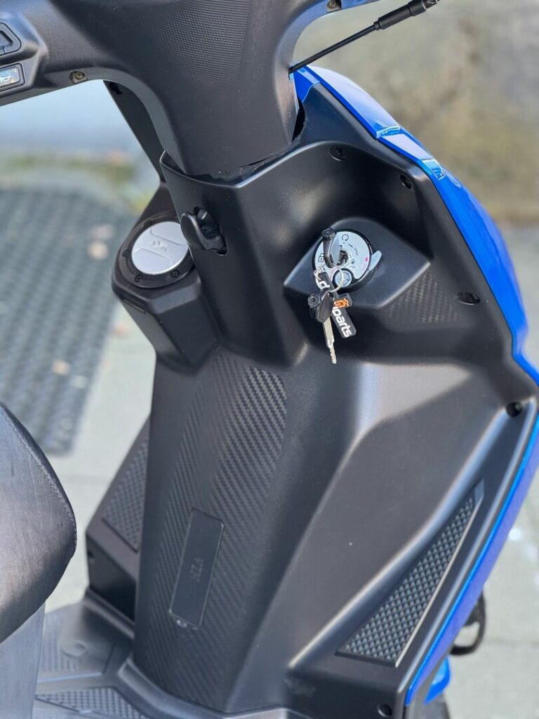 Close-up van een blauwe scooter: sleutel in het contactslot op de middenconsole met zwarte panelen.