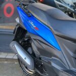 Close-up van de achterzijde van een blauwe scooter met zwarte zitting, uitlaat en bagagerek; Orbit III logo.