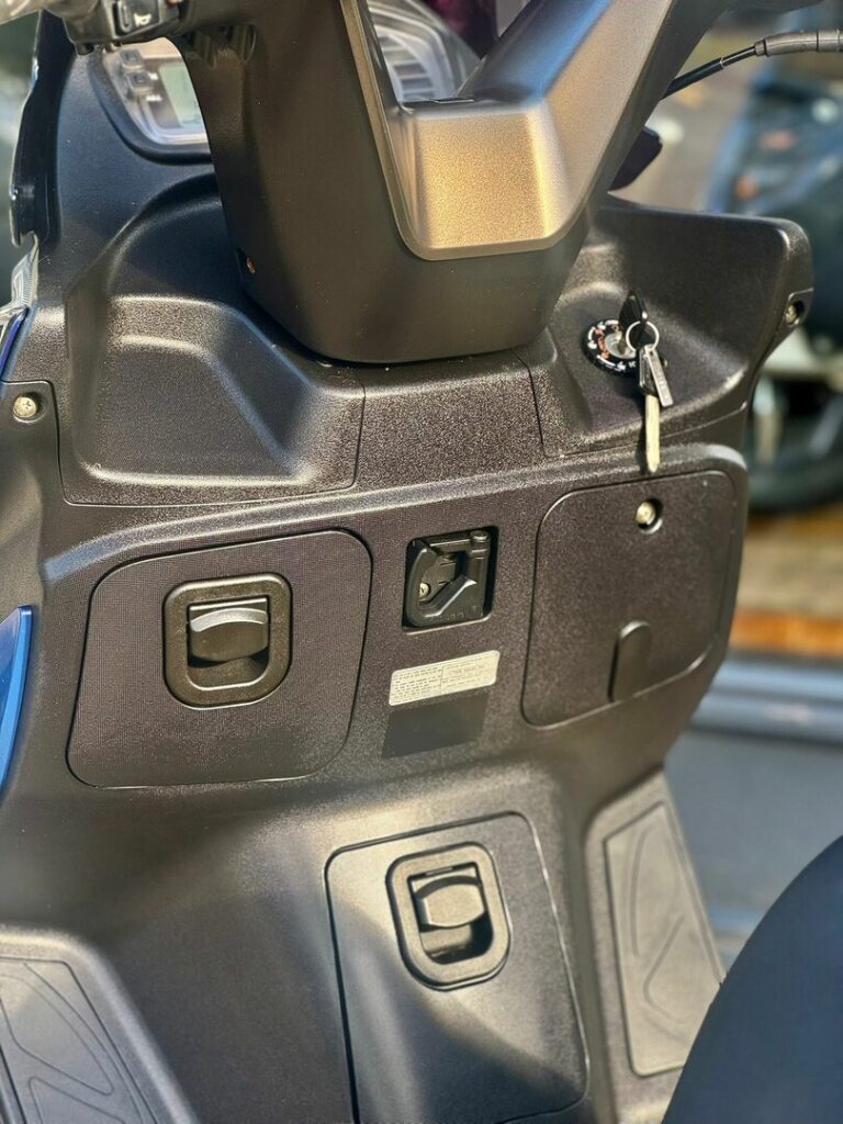 Close-up van het stuur en de middenconsole van een scooter met contactsleutel en opbergvakken.