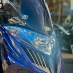 Close-up van de voorkant van een blauwe scooter met hoog windscherm en koplamp.