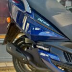 Close-up van de achterkant van een blauwe scooter met zadel, uitlaat en achterwiel.