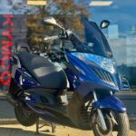 Blauwe Kymco-scooter op standaard voor een winkel met glazen pui.
