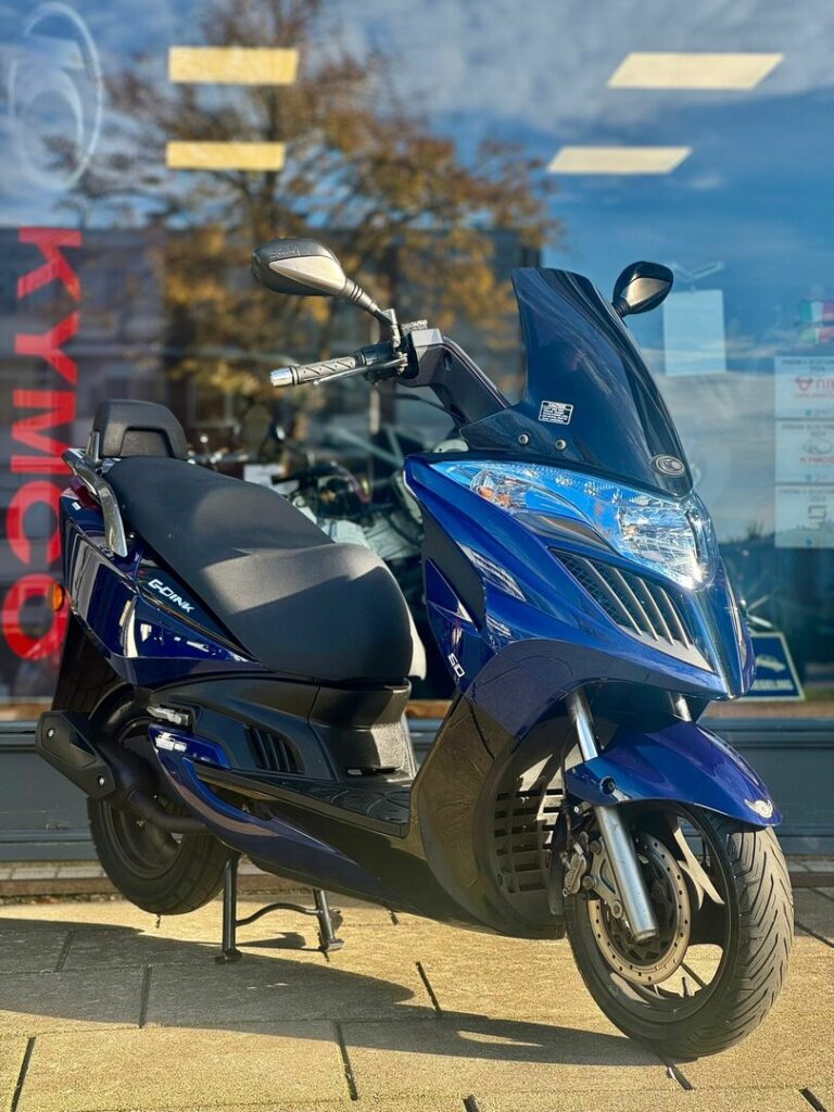 Blauwe Kymco-scooter op standaard voor een winkel met glazen pui.