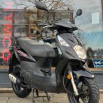 Zwarte scooter op middenbok voor een winkelruit met weerspiegeling