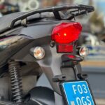 Achterzijde van een scooter met brandend achterlicht, richtingaanwijzers en blauwe NL-kentekenplaat.