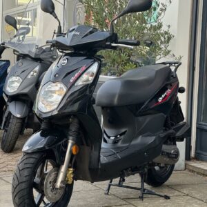 Zwarte SYM Orbit II scooter op standaard voor een winkel, schuin van voren.