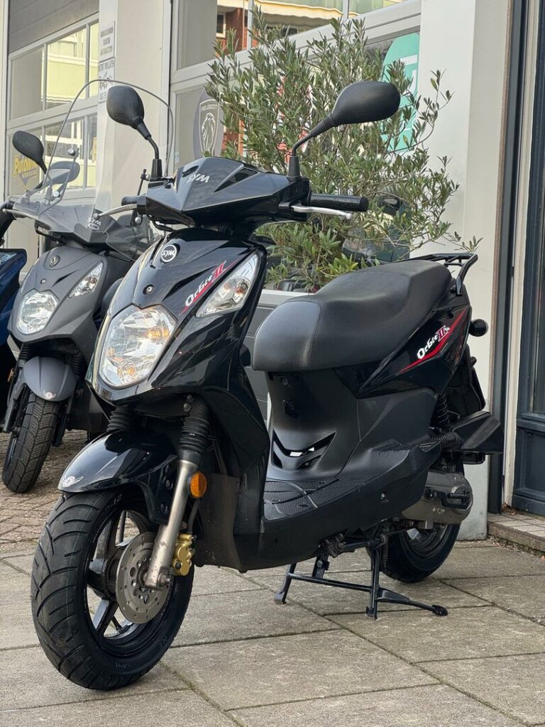 Zwarte SYM Orbit II scooter op standaard voor een winkel, schuin van voren.