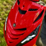 Close-up van de rode voorkap van een sportieve scooter met LED-dagrijlichten en Malossi-sticker.