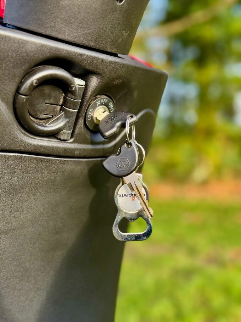 Scootersleutels in het contactslot, close-up van een zwarte scooter met flesopener-sleutelhanger buiten.