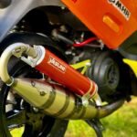 Close-up van een Yasuni racinguitlaat op een oranje scooter met Malossi- en MHR-stickers.