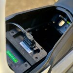 Close-up van de Super Soco elektrische scooteraccu met aangesloten laadkabel in het zadelvak.