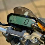 Close-up van een motorstuur met digitaal dashboard van Super Soco, snelheid 0 km/u zichtbaar.