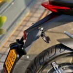 Achterzijde van een motorfiets met rode achterlicht, knipperlicht en gele kentekenplaat.