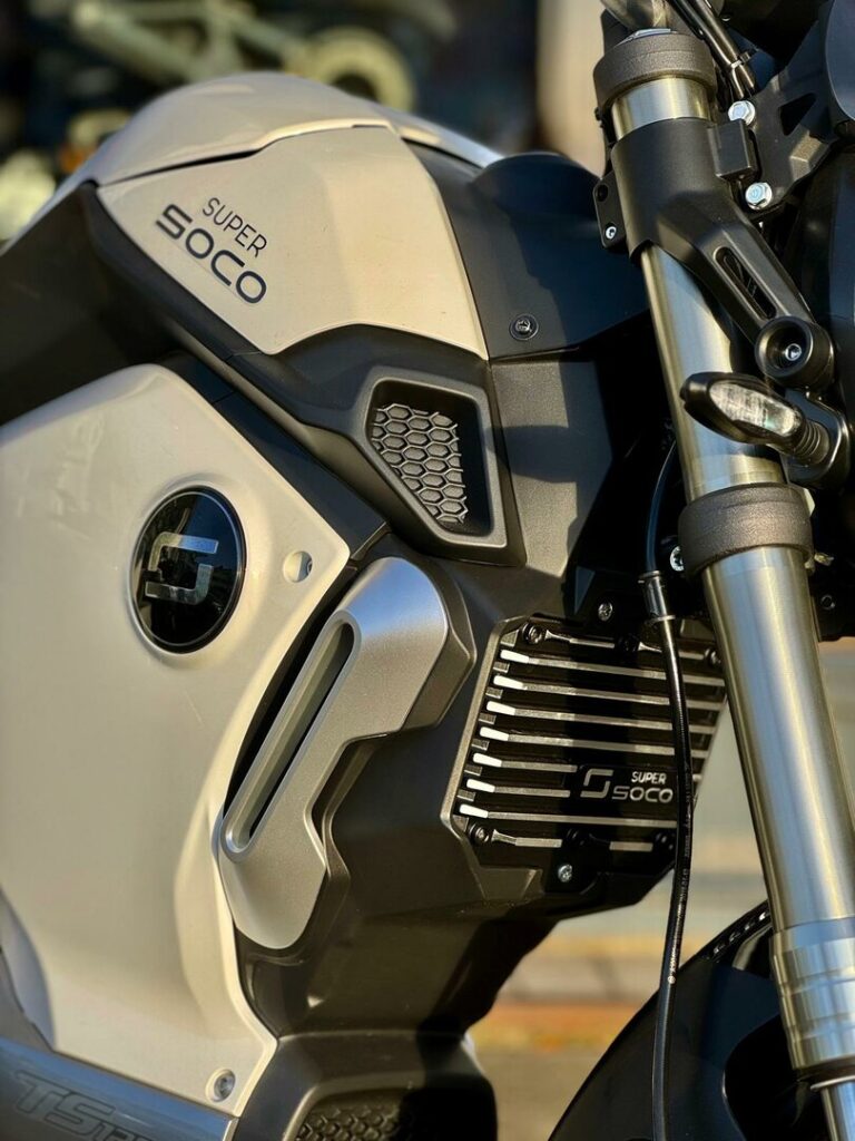 Close-up van een Super Soco elektrische motor met voorvork, ventilatieroosters en logo.