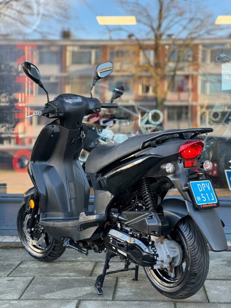 Zwarte scooter op standaard met blauwe kentekenplaat voor een winkelruit.