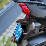 Close-up van de achterzijde van een zwarte SYM-scooter met bagagedrager, achterlicht en blauwe kentekenplaat.