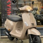 Beige retro scooter op standaard voor een winkel, met brandende koplamp.