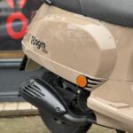 Close-up van de beige AGM VX50i scooter, met zadel, uitlaat en oranje reflector bij het achterwiel.