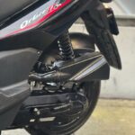 Close-up van de achterzijde van een zwarte scooter met vering, motorbehuizing en achterwiel.