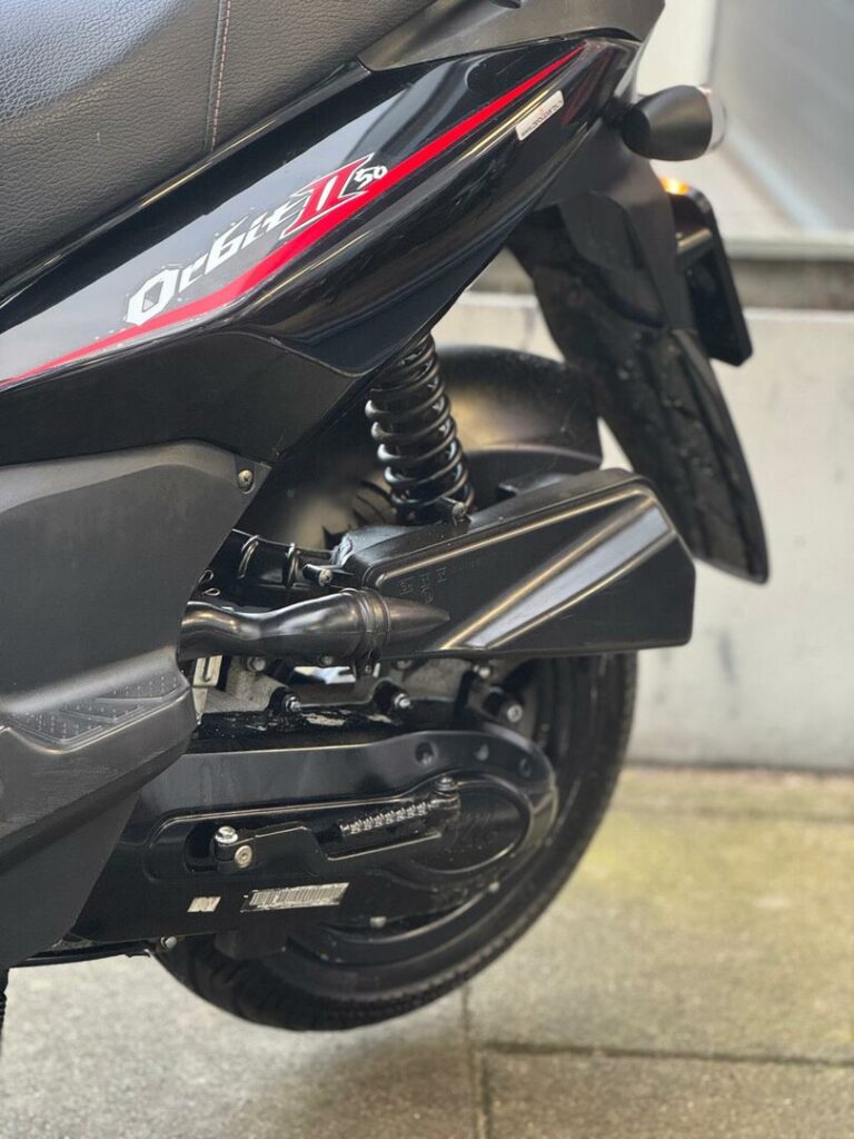 Close-up van de achterzijde van een zwarte scooter met vering, motorbehuizing en achterwiel.