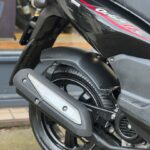 Close-up van het achterwiel en de uitlaat van een zwarte scooter met rode striping.