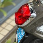 Close-up van het rode achterlicht, chroomdetails en blauwe kentekenplaat van een scooter.