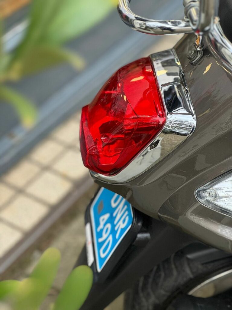 Close-up van het rode achterlicht, chroomdetails en blauwe kentekenplaat van een scooter.