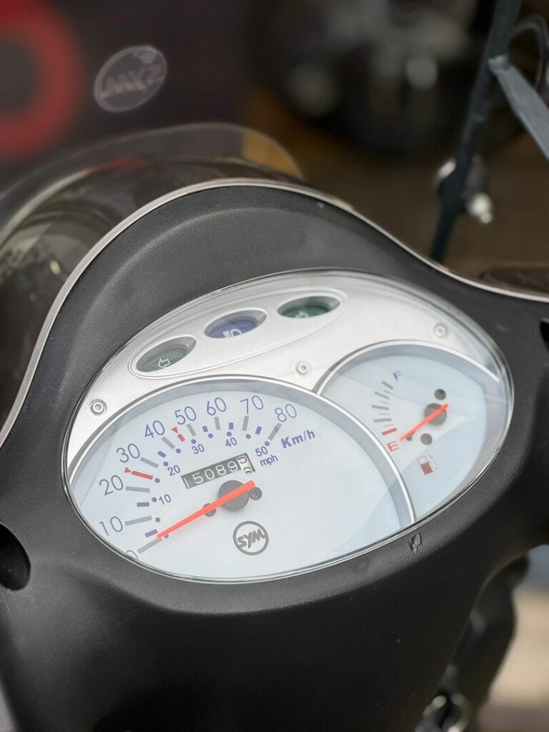 Close-up van het dashboard van een SYM scooter met snelheidsmeter en brandstofmeter.
