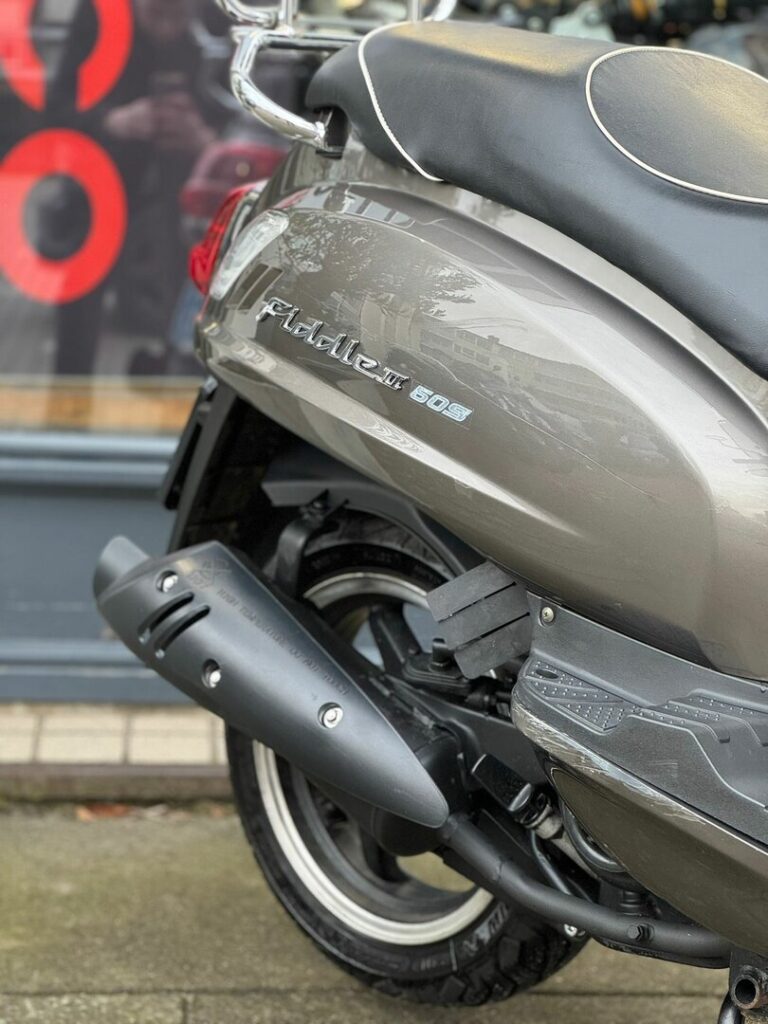 Close-up van de achterzijde van een grijze scooter met uitlaat, zadel en Fiddle III 50S-logo.