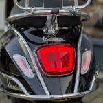 Achterkant van een zwarte Vespa-scooter met rood achterlicht en chromen bagagedrager.