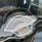 Close-up van het dashboard en de snelheidsmeter van een zwarte Vespa scooter.