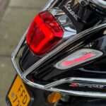 Close-up van de achterkant van een zwarte Vespa Sprint met rood achterlicht, chroomrek en gele kentekenplaat.