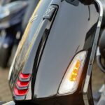 Close-up van de glanzende voorkant van een zwarte scooter met brandend oranje knipperlicht en rode accenten.