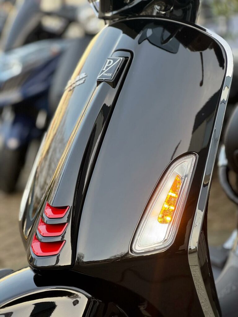 Close-up van de glanzende voorkant van een zwarte scooter met brandend oranje knipperlicht en rode accenten.
