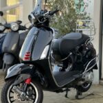 Glanzend zwarte scooter met ruitje en rood geveerde voorvork, geparkeerd bij een winkel.