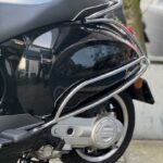 Detaillaanzicht van de achterzijde van een zwarte scooter met chromen valbeugels en bagagerek.