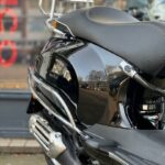 Close-up van de achterkant van een zwarte scooter met chromen bagagedrager en uitlaat.