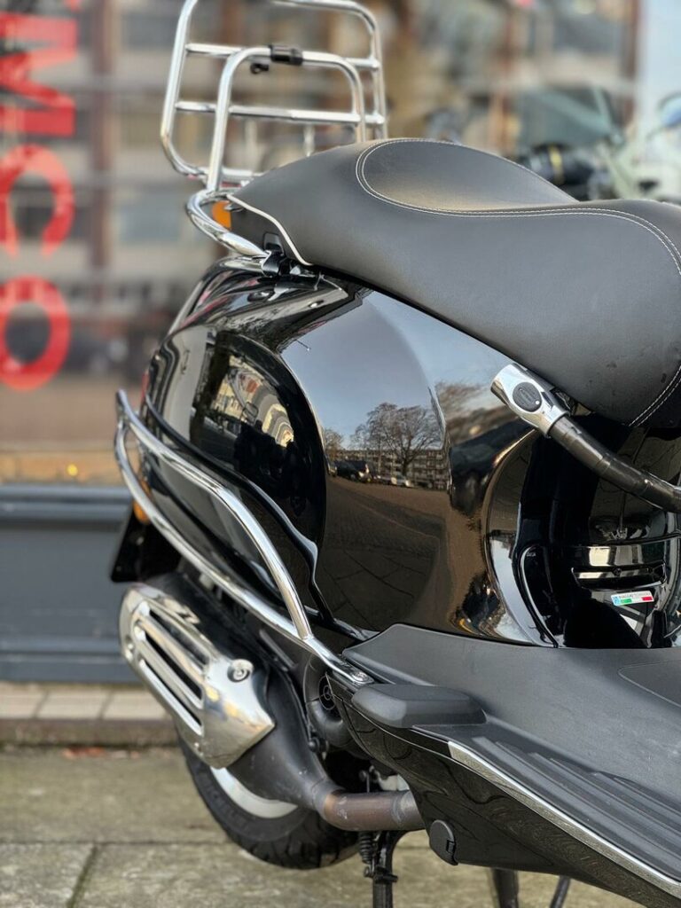 Close-up van de achterkant van een zwarte scooter met chromen bagagedrager en uitlaat.