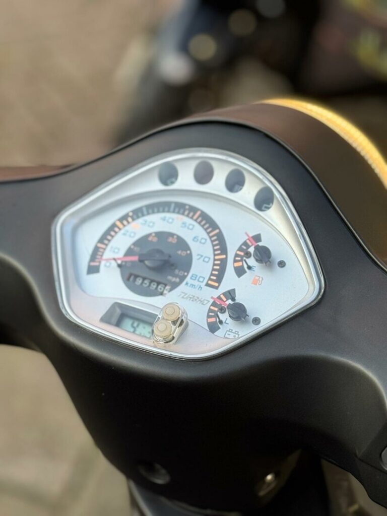 Close-up van het dashboard van een scooter met snelheidsmeter en brandstofmeter.