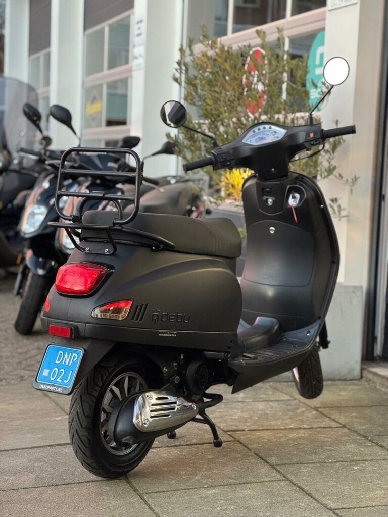 Zwarte scooter met bagagedrager, op standaard geparkeerd voor een scooterdealer.