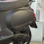 Close-up van de achterzijde van een matzwarte scooter met bagagerek en zichtbaar achterwiel.