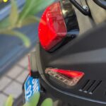 Close-up van de achterzijde van een scooter met brandend achterlicht en knipperlicht, blauwe kentekenplaat.