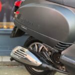 Close-up van de achterzijde van een matte zwarte scooter met uitlaat, achterwiel en zadel.