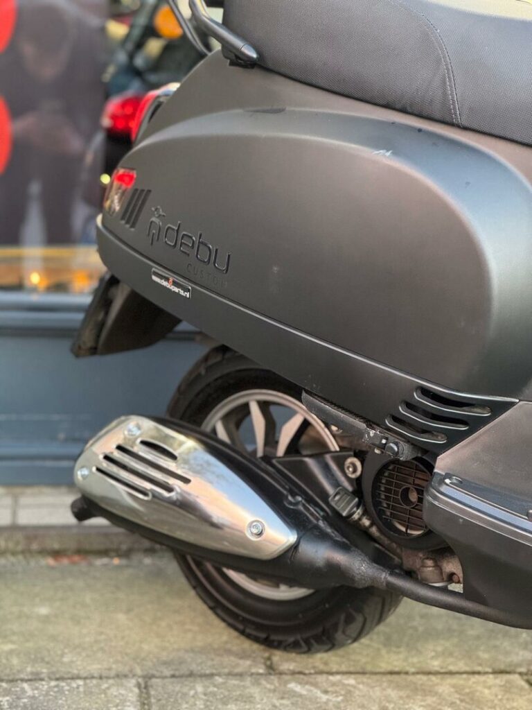Close-up van de achterzijde van een matte zwarte scooter met uitlaat, achterwiel en zadel.
